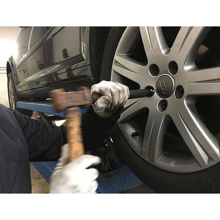 the mechanic is seen striking the wheel nut removal tool being used on a car wheel with a hammer